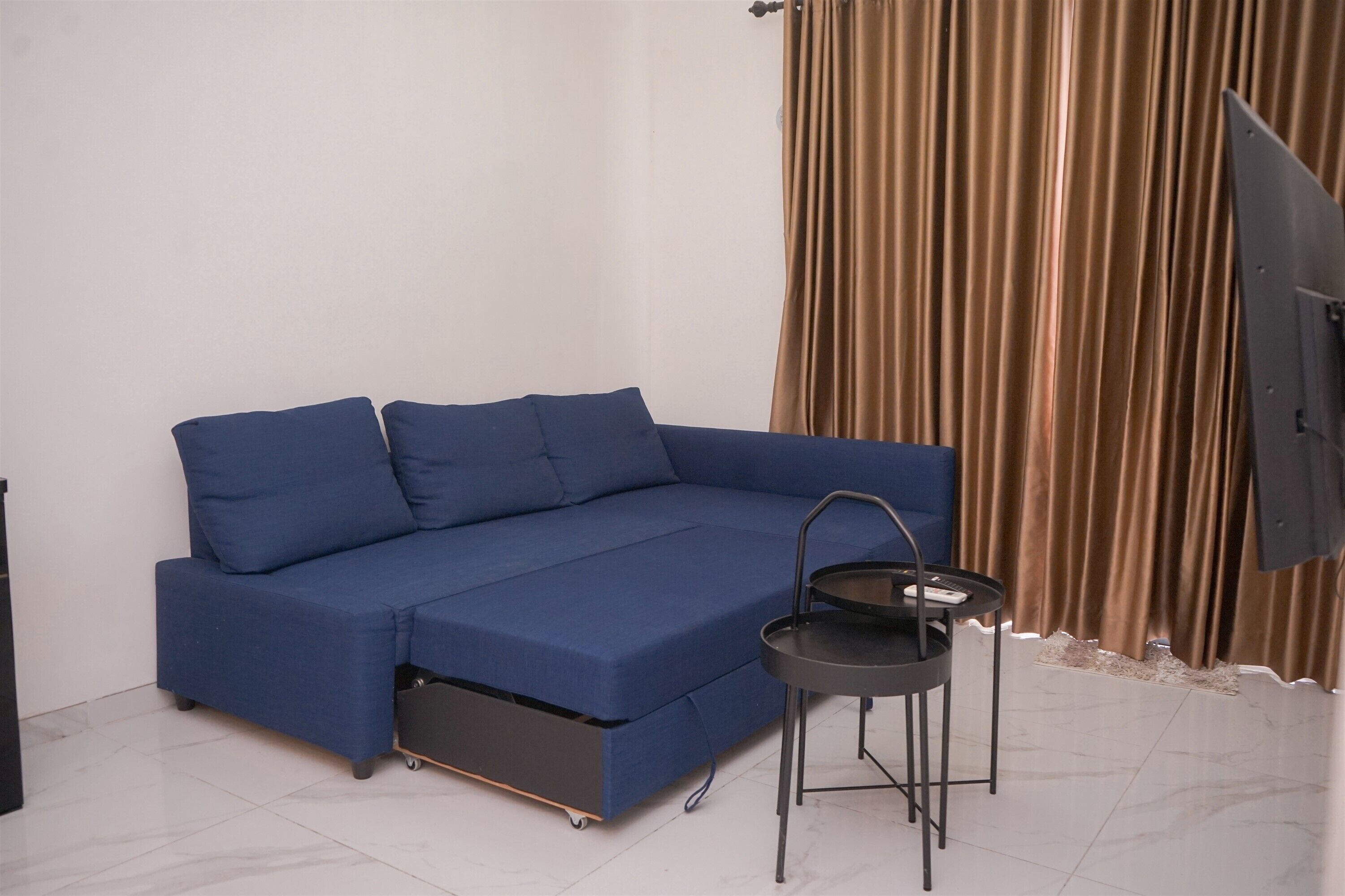 A blue sofa with a pull-out bed, a small table, and a curtain.