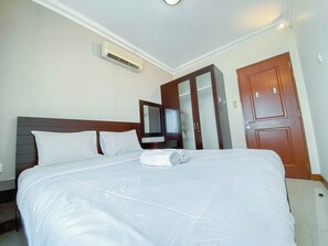 Ein Hotelzimmer mit einem ordentlich bezogenen Bett, einem Kleiderschrank, einem Spiegel und einer Klimaanlage.