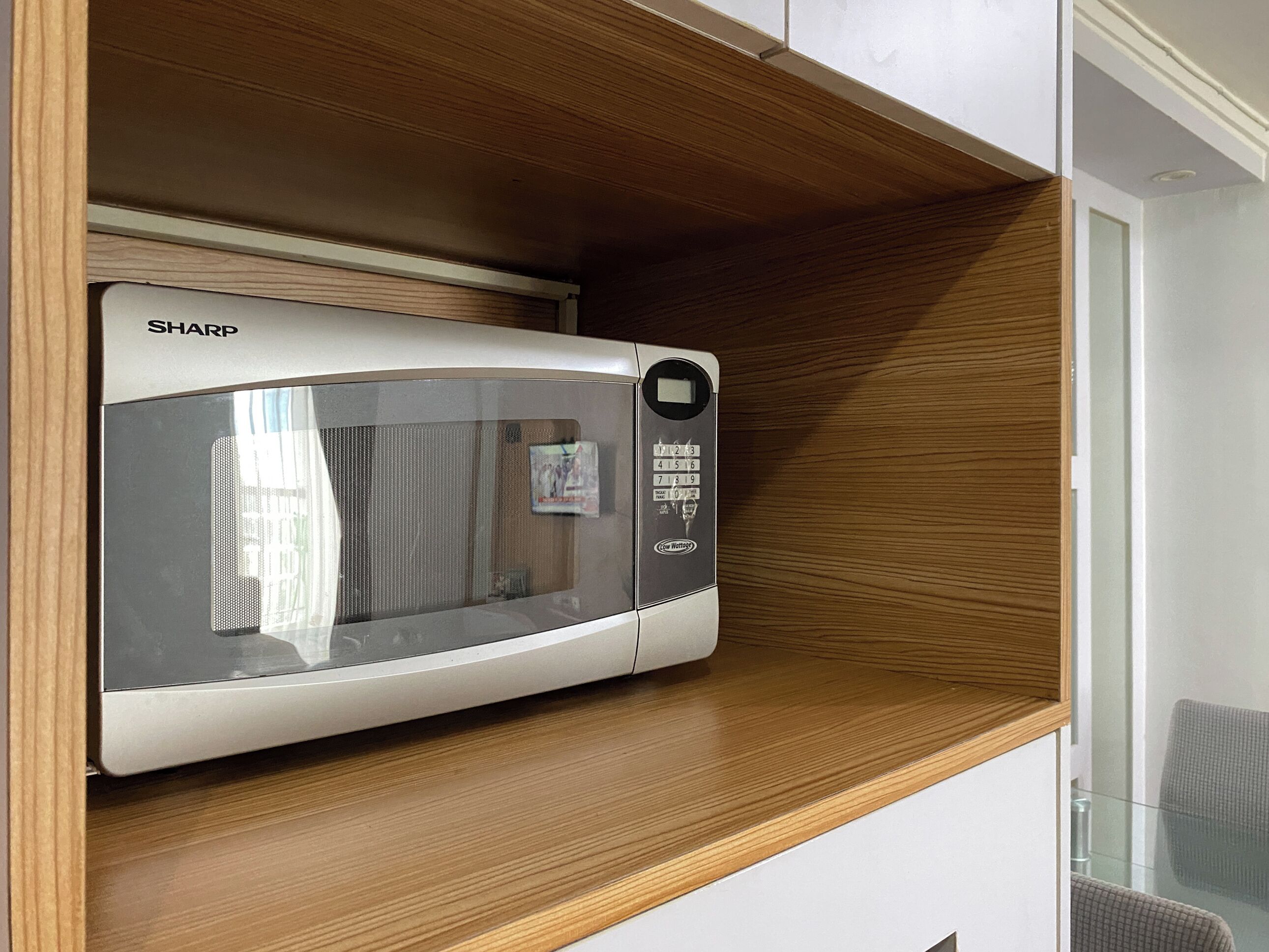 A microwave oven on a wooden shelf in a kitchen.