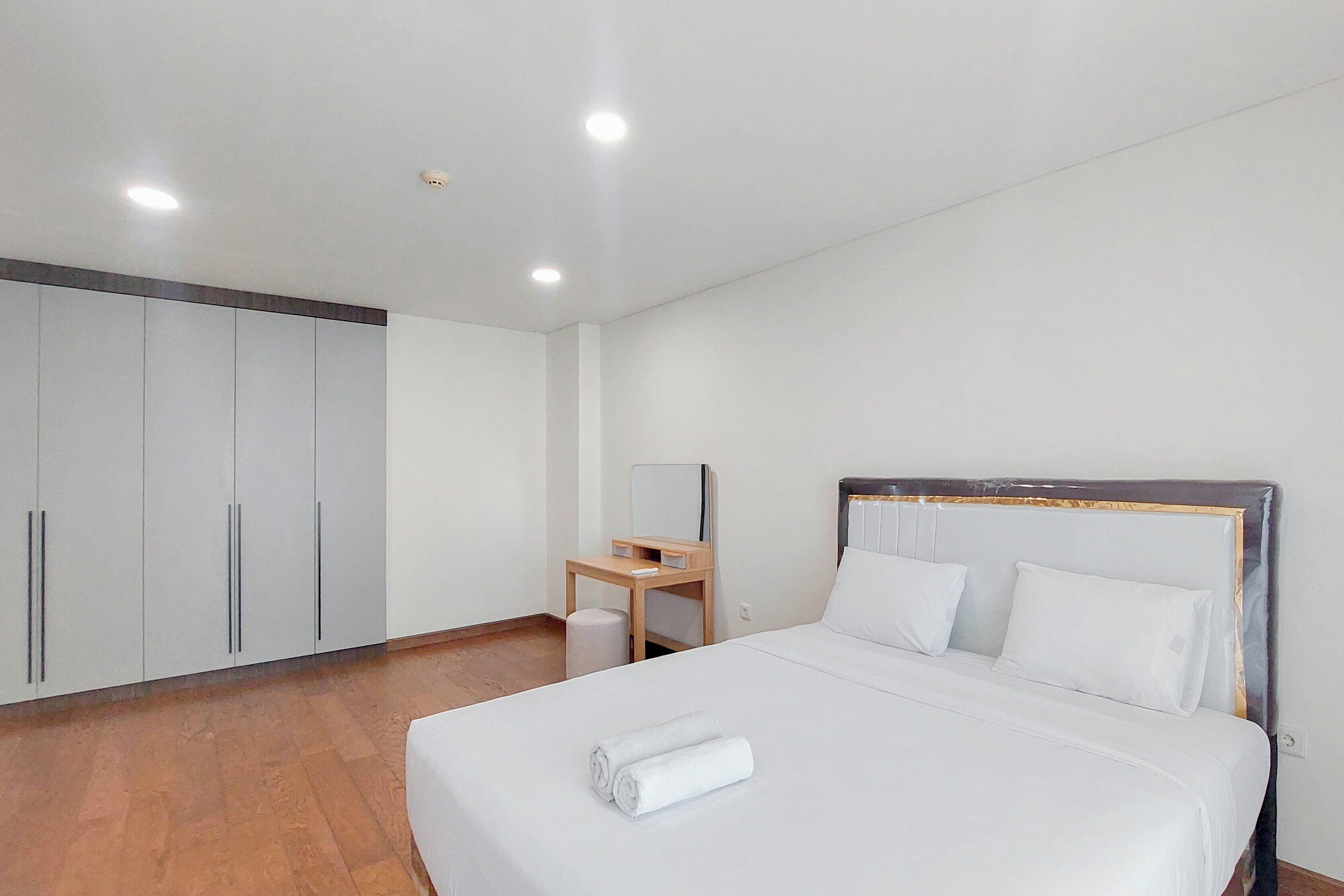 Quarto de hotel com cama, mesa de cabeceira de madeira, espelho e guarda-roupa.
