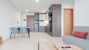 Egy modern nappali, szürke színű kanapéval, egy fa kávézóasztallal, valamint egy étkezővel, melyben két szék és egy asztal található.