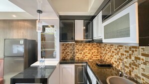 A modern kitchen with black countertops, white cabinets, a built-in microwave, and a tiled backsplash. - 1BR Modern Suites at Tamansari Prospero Sidoarjo Apartment (Sidoarjo)