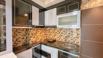 A compact kitchen with white cabinets, a black countertop, and a mosaic backsplash.