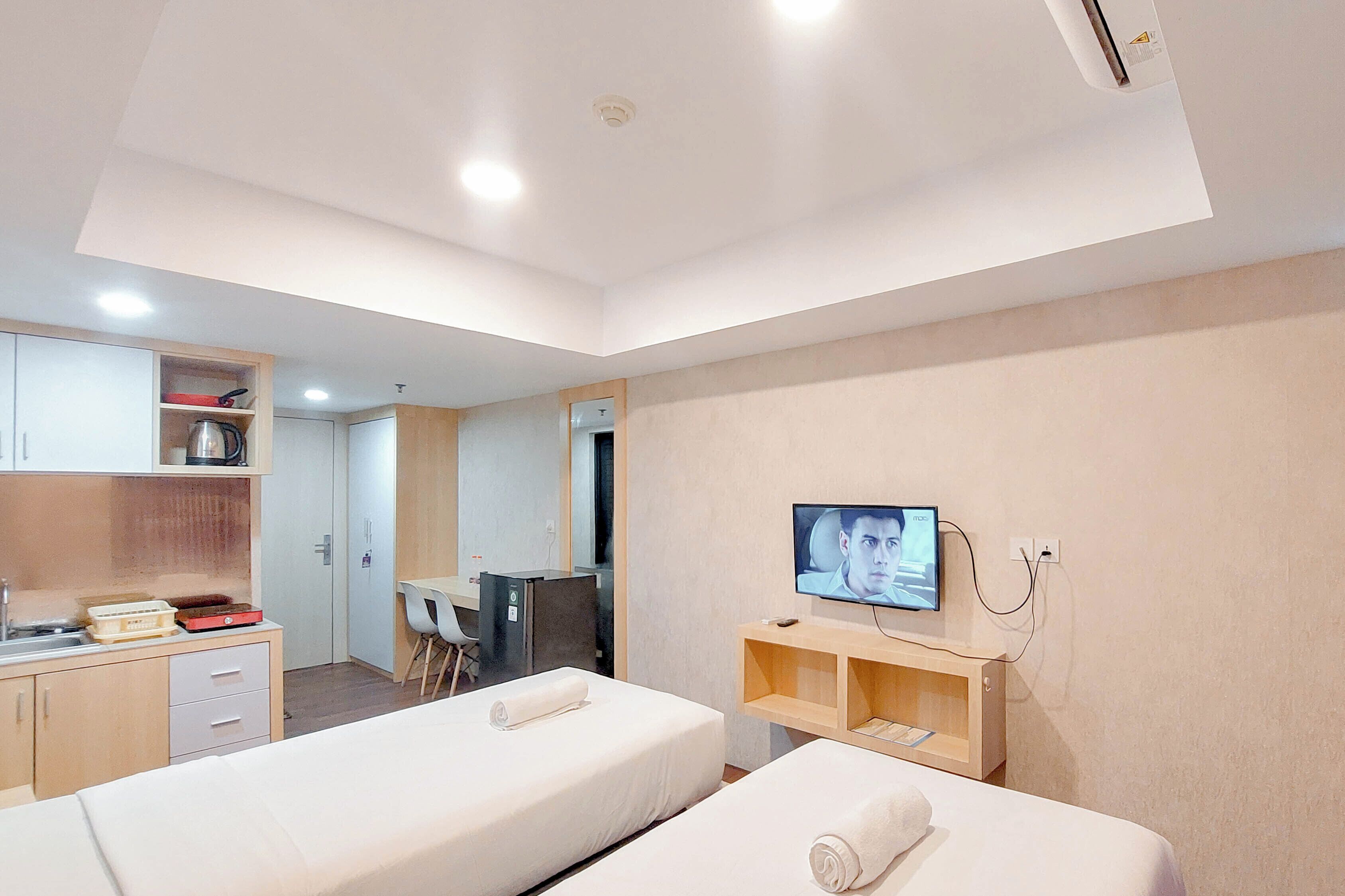 A hotel room with two beds, a TV, a desk, and a kitchenette.