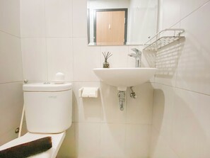 A modern bathroom with a toilet, sink, and a mirror above the sink. - Comfort Living Studio at Monroe Tower Apartment (Cikarang)