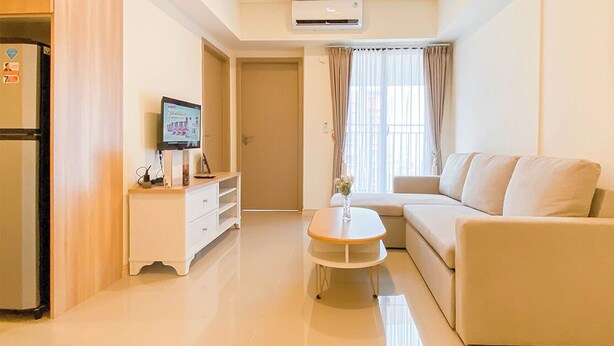 A modern living room with a beige sofa, a small round table, a white cabinet, and a television on a stand. - Cozy Place and Tidy 2BR Apartment Meikarta (Cikarang)