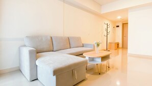A modern living room with a light-colored sectional sofa, a small round table, and a vase with flowers. - Cozy Place and Tidy 2BR Apartment Meikarta (Cikarang)