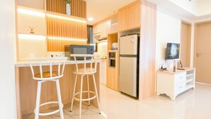 A modern kitchen with a central island, two bar stools, a refrigerator, and a television on a stand. - Cozy Place and Tidy 2BR Apartment Meikarta (Cikarang)