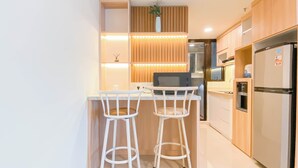 A modern kitchen with two white bar stools, wooden cabinets, a stainless steel refrigerator, and a built-in microwave. - Cozy Place and Tidy 2BR Apartment Meikarta (Cikarang)