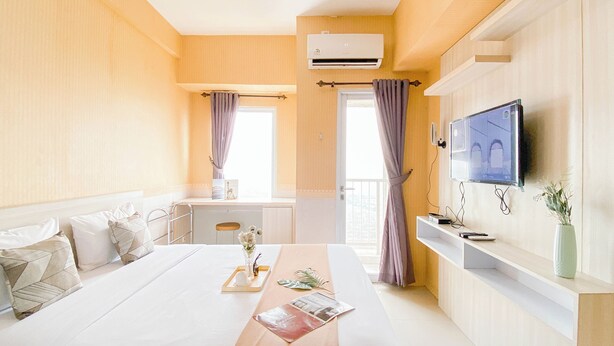 A modern hotel room with a large bed, a desk, a television, and a balcony with curtains.