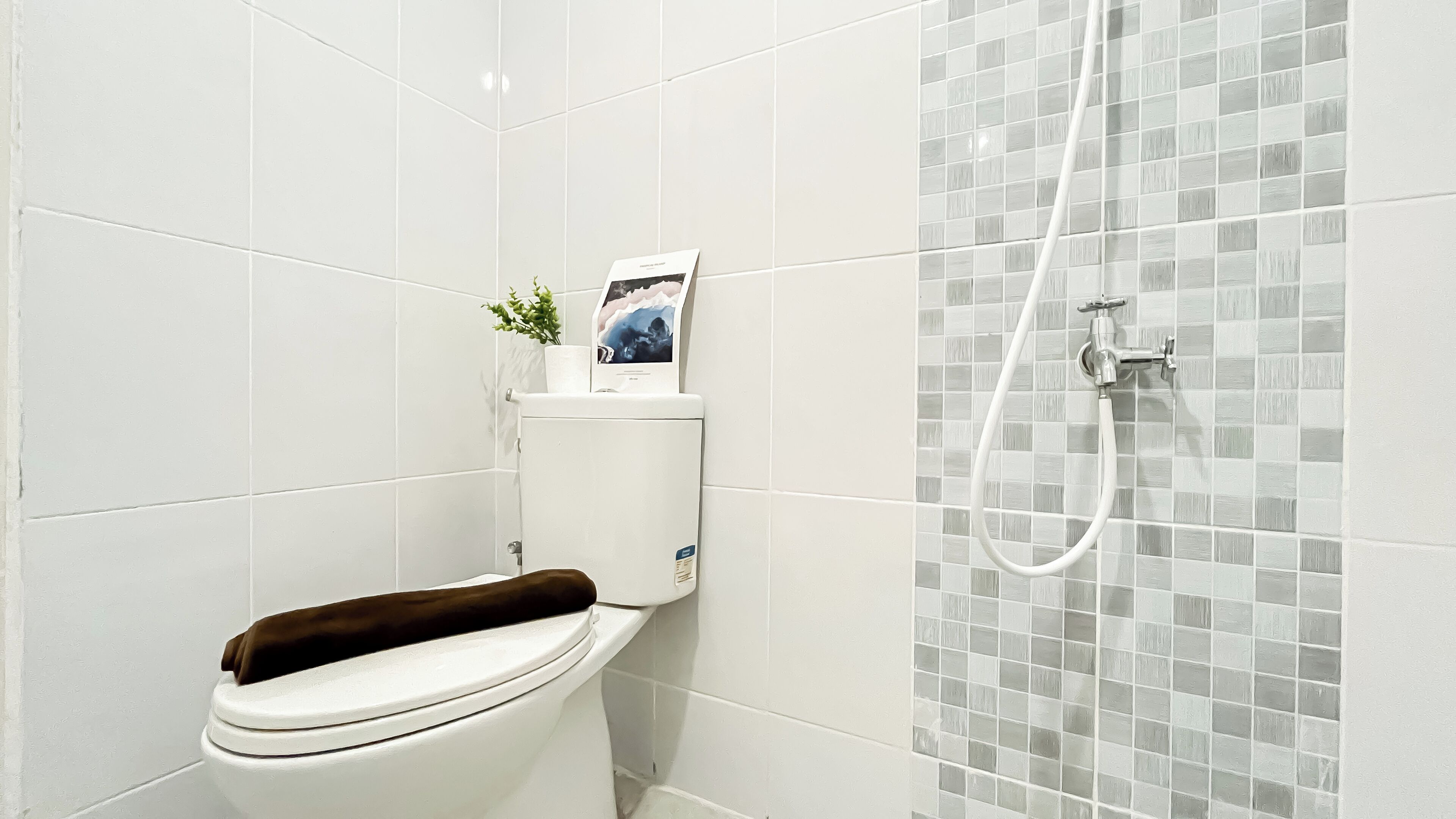 A bathroom with a toilet, a shower, and a tiled wall.