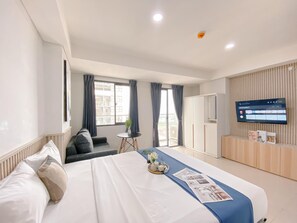 A modern hotel room with a large bed, a television mounted on the wall, a small table with a plant, and a view of the outside balcony. - Fully Furnished and Cozy Studio Daan Mogot City Apartment (Jakarta)