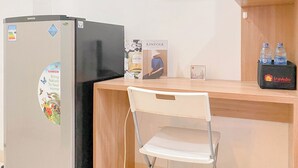 Eine Küchenzeile mit Kühlschrank, einem Sessel und einem Regal mit Wasserflaschen und einer Reisetasche.