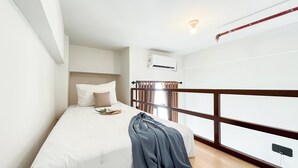 Une chambre à coucher comprenant un lit, une table de chevet, une fenêtre avec des rideaux, un appareil de climatisation et une vue sur l’extérieur.