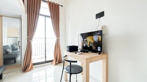 Une chambre moderne dotée d’une grande fenêtre, d’un téléviseur à écran plat, d’un bureau en bois, d’une chaise noire et d’un canapé gris.