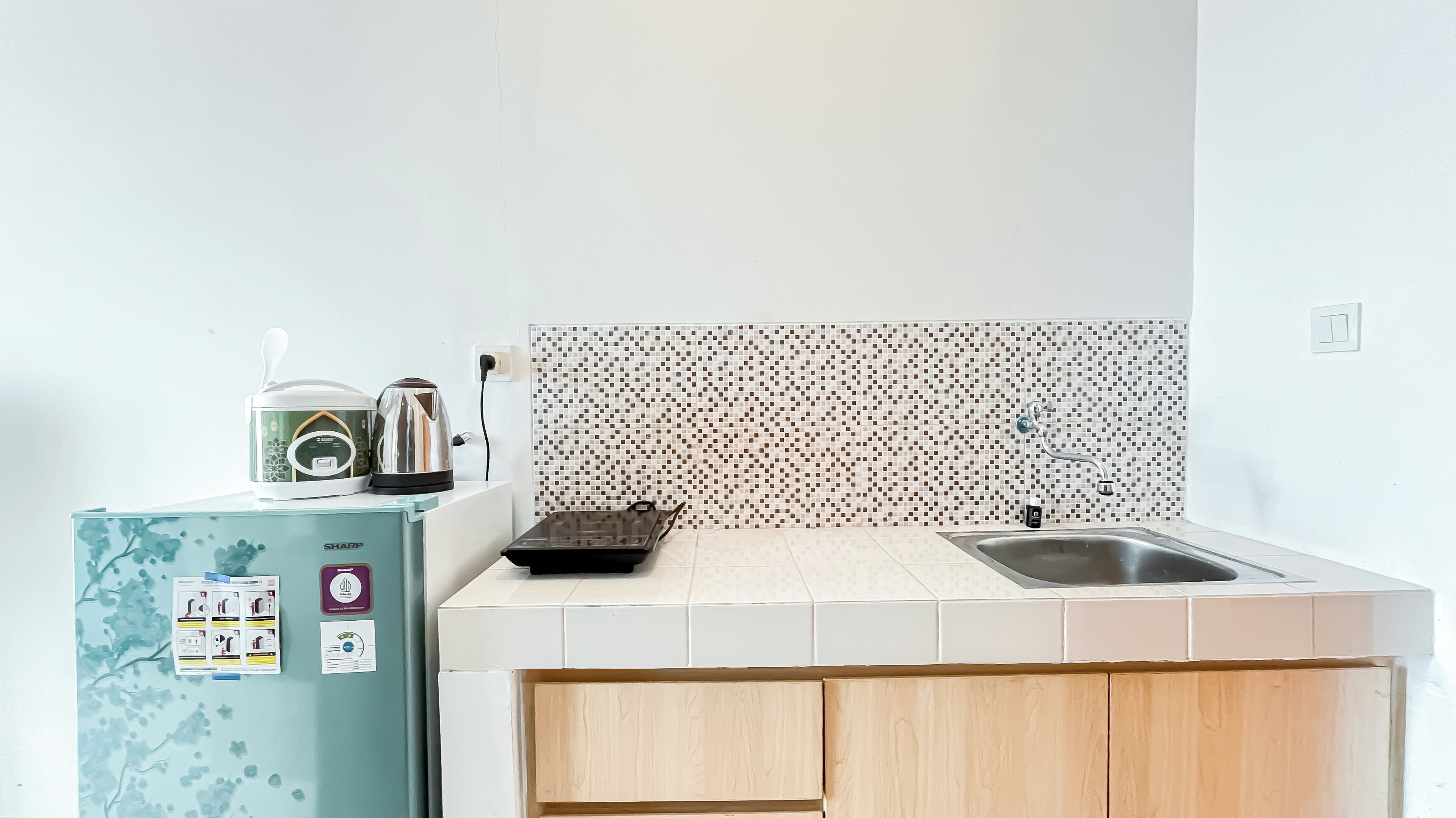 A compact kitchen with a refrigerator, a kettle, a coffee maker, and a sink.