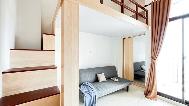 Une pièce moderne avec un canapé gris, un escalier en bois et une grande fenêtre avec des rideaux.