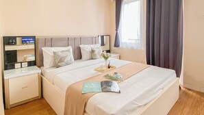 A hotel room with a bed, bedside tables, a TV, and a window with curtains. - Warm and Cozy 1BR without Living Room at Sentul Tower Apartment (Citaringgul)