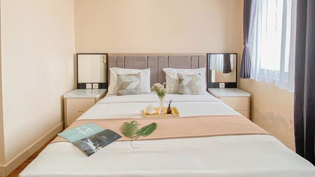 A hotel room with a large bed, two bedside tables, a mirror, and a window with curtains. - Warm and Cozy 1BR without Living Room at Sentul Tower Apartment (Citaringgul)