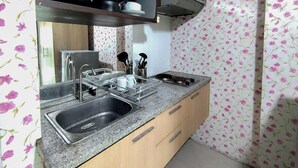 A kitchen with a stainless steel sink, a granite countertop, wooden cabinets, and a backsplash with a floral pattern. - Comfy and Warm Studio at The Square Surabaya Apartment (Surabaya)