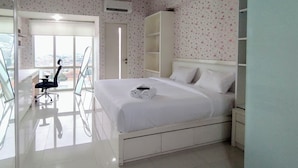 A hotel room with a bed, a desk, and a chair. There is a window with a view of buildings outside. - Comfy and Warm Studio at The Square Surabaya Apartment (Surabaya)