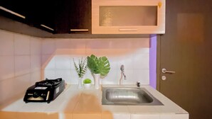 A kitchen with a white countertop, a stainless steel sink, a microwave, and a small potted plant.