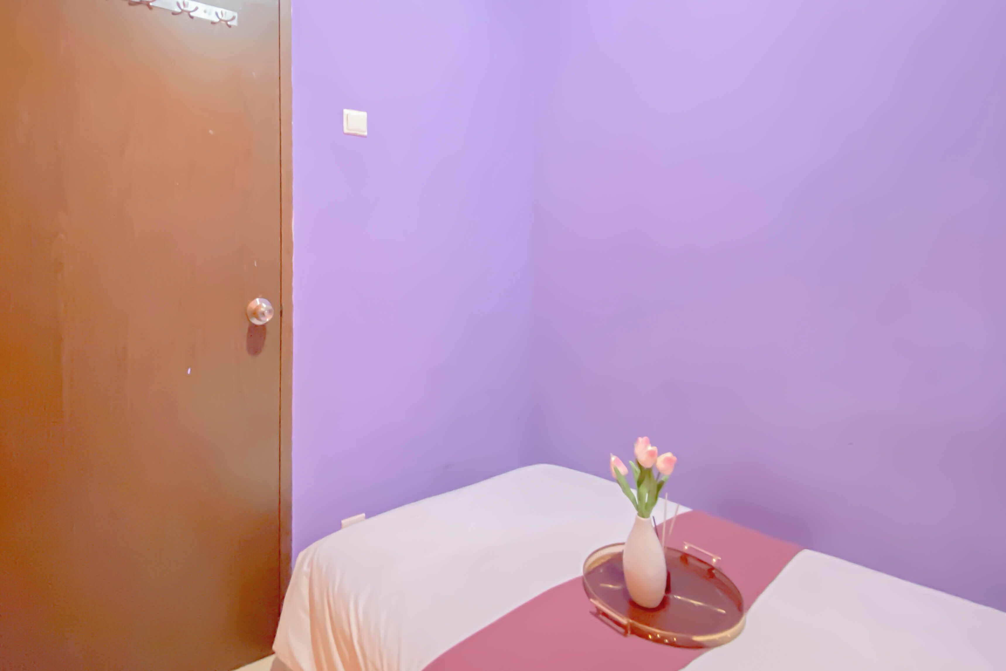 Ein Zimmer mit einem Bett, einer Tür und einer Tischvase mit Blumen.