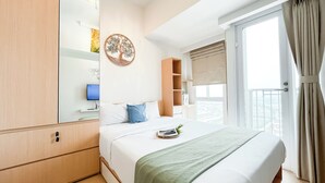 Ein Hotelzimmer mit Bett, Fernseher, Kleiderschrank und einem großen Fenster mit Vorhängen.