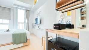 Egy szállodai szoba, amelyben található egy ágy, egy íróasztal számítógéppel, egy szék, egy televízió és egy minibar.
