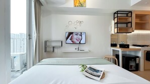 Ein Hotelzimmer mit Bett, einem an der Wand befestigten Fernseher, einem kleinen Tisch mit Pflanze und Blick auf die Stadt.