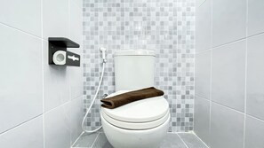 Egy modern fürőszoba, amelyben található egy WC, WC-papírtartó és egy zuhanycső.
