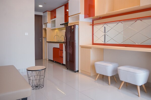 Cocina moderna con refrigerador, pileta y muebles color naranja. Hay dos taburetes blancos y una mesa redonda con estructura de alambre.