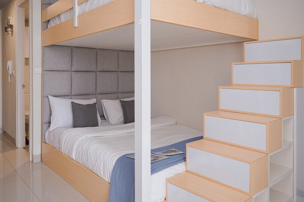 A bunk bed with a grey headboard, a white mattress, and a blue blanket. There is a wooden staircase with white panels leading to a landing. - Combined and Spacious 1BR Apartment at Parkland Avenue (South Tangerang)