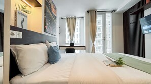 A hotel room with a bed, a desk, a chair, a TV, and a window with curtains. - Comfort and Tidy Studio at Tokyo Riverside PIK 2 Apartment (Teluknaga)