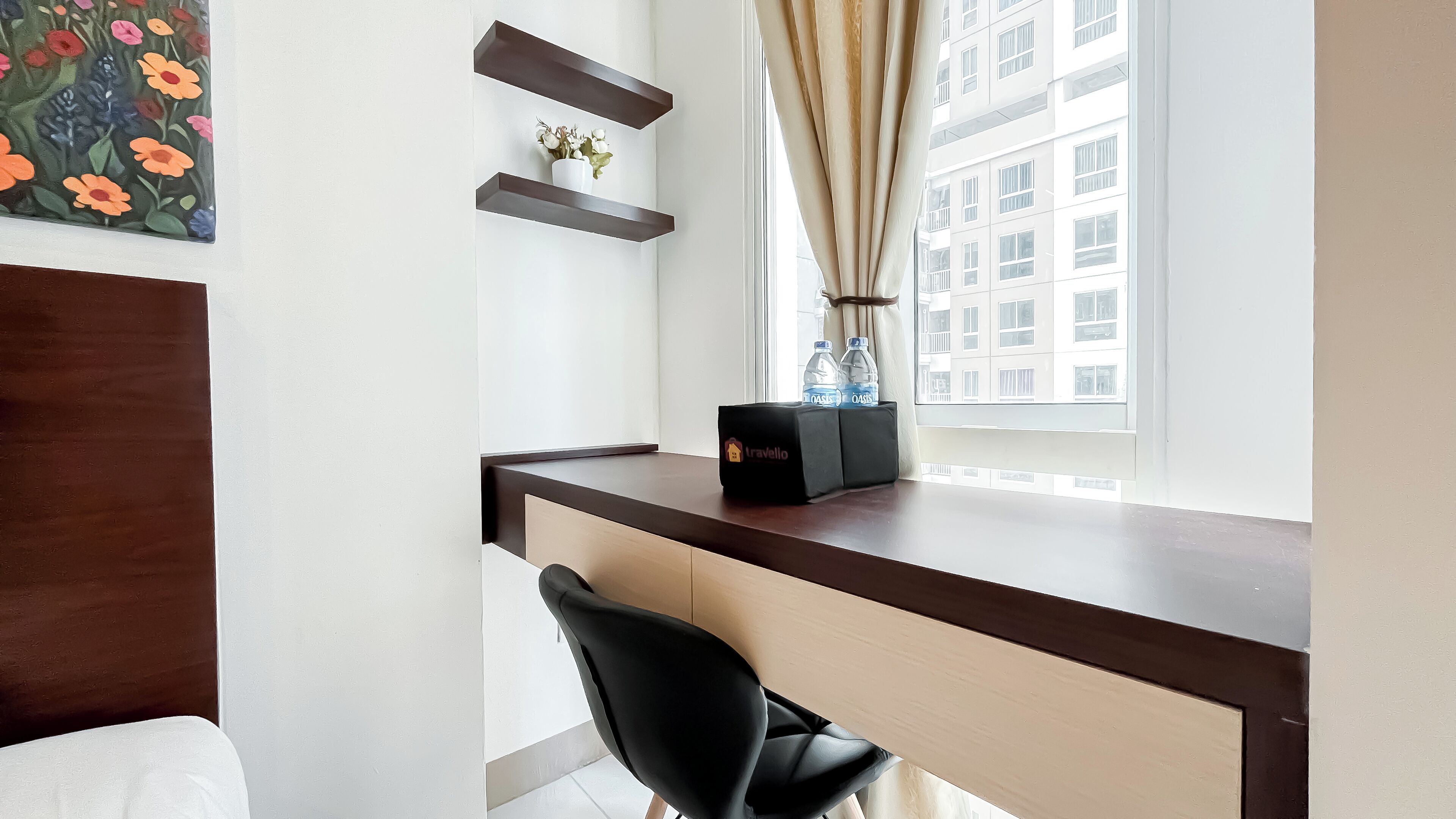 Une chambre d’hôtel moderne avec un bureau en bois, une chaise noire, une petite plante en pot et une fenêtre avec des rideaux.