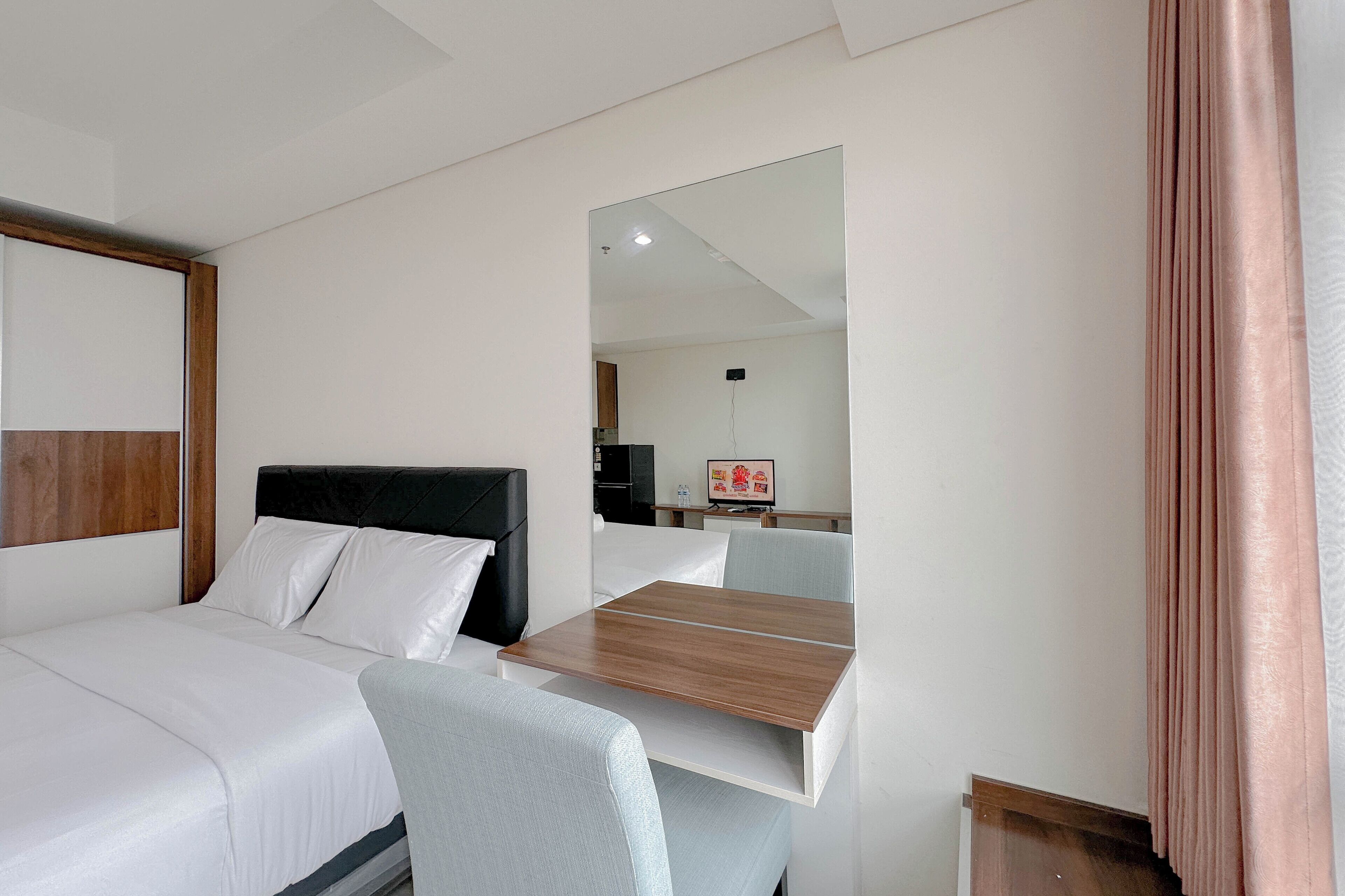 A hotel room with a bed, a desk, a chair, and a mirror.