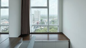 A modern room with large windows, a wooden bench, and a view of a cityscape. - Tidy and Strategic Location Studio Grand Sungkono Lagoon Apartment (Surabaya)