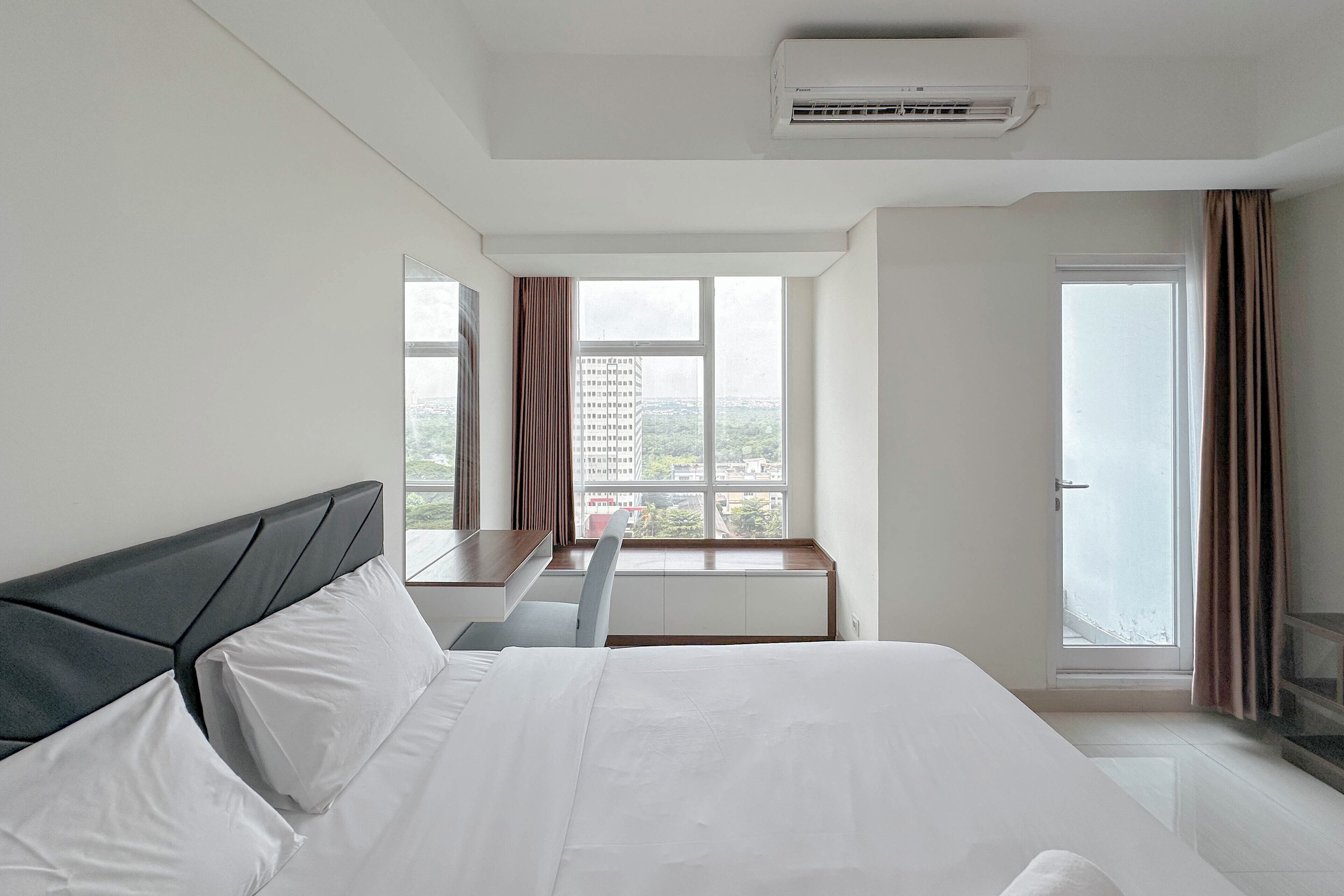 A hotel room with a large bed, a desk, and a window with a view of buildings.