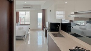 A modern hotel room with a bed, a kitchenette, and a view of the cityscape. - Tidy and Strategic Location Studio Grand Sungkono Lagoon Apartment (Surabaya)