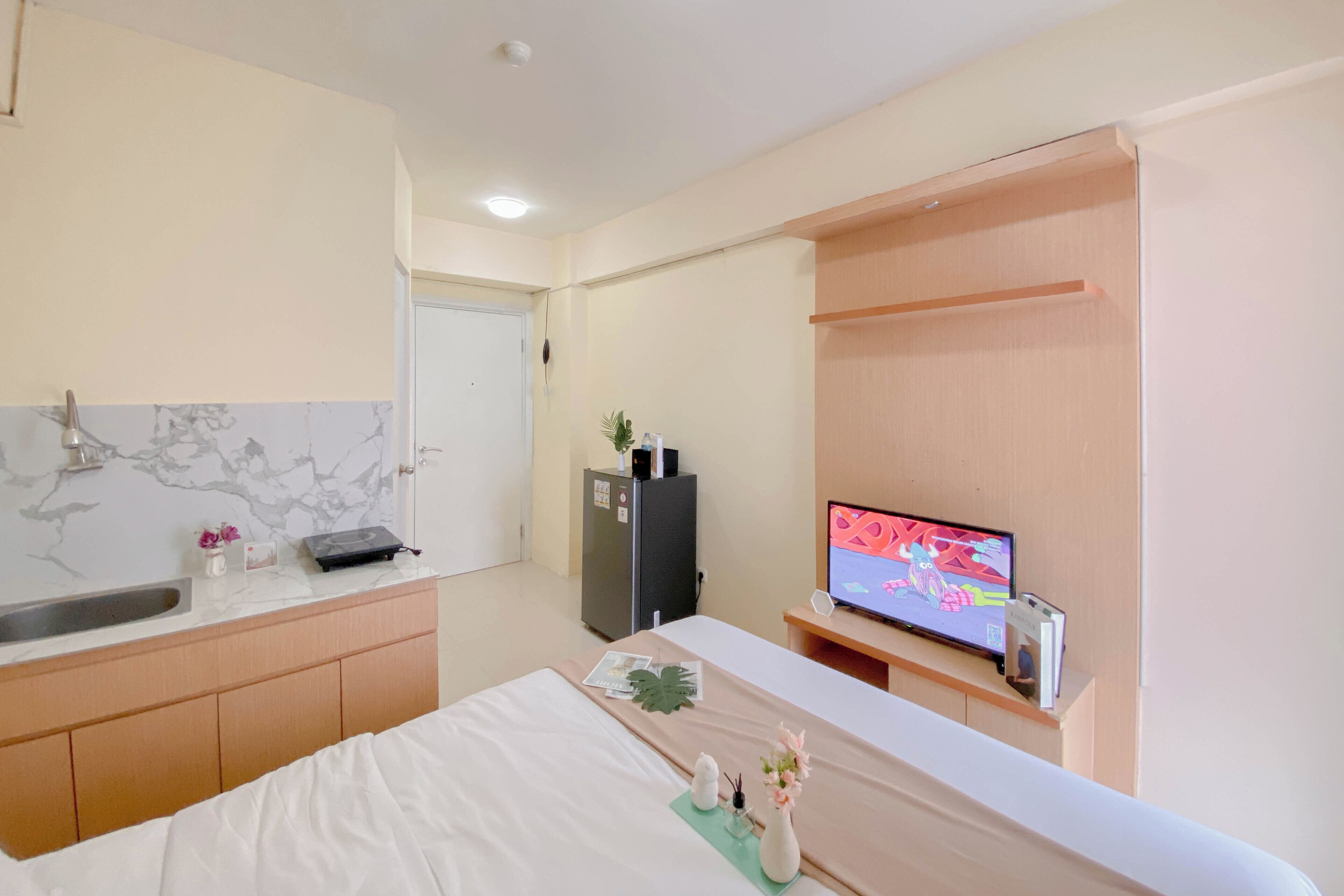 A hotel room with a bed, a small kitchenette, a television, and a desk.