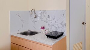A kitchen with a marble backsplash, a sink, a stove, and wooden cabinets. - Nice Studio Green Pramuka City Apartment near Shopping Center (Jakarta)