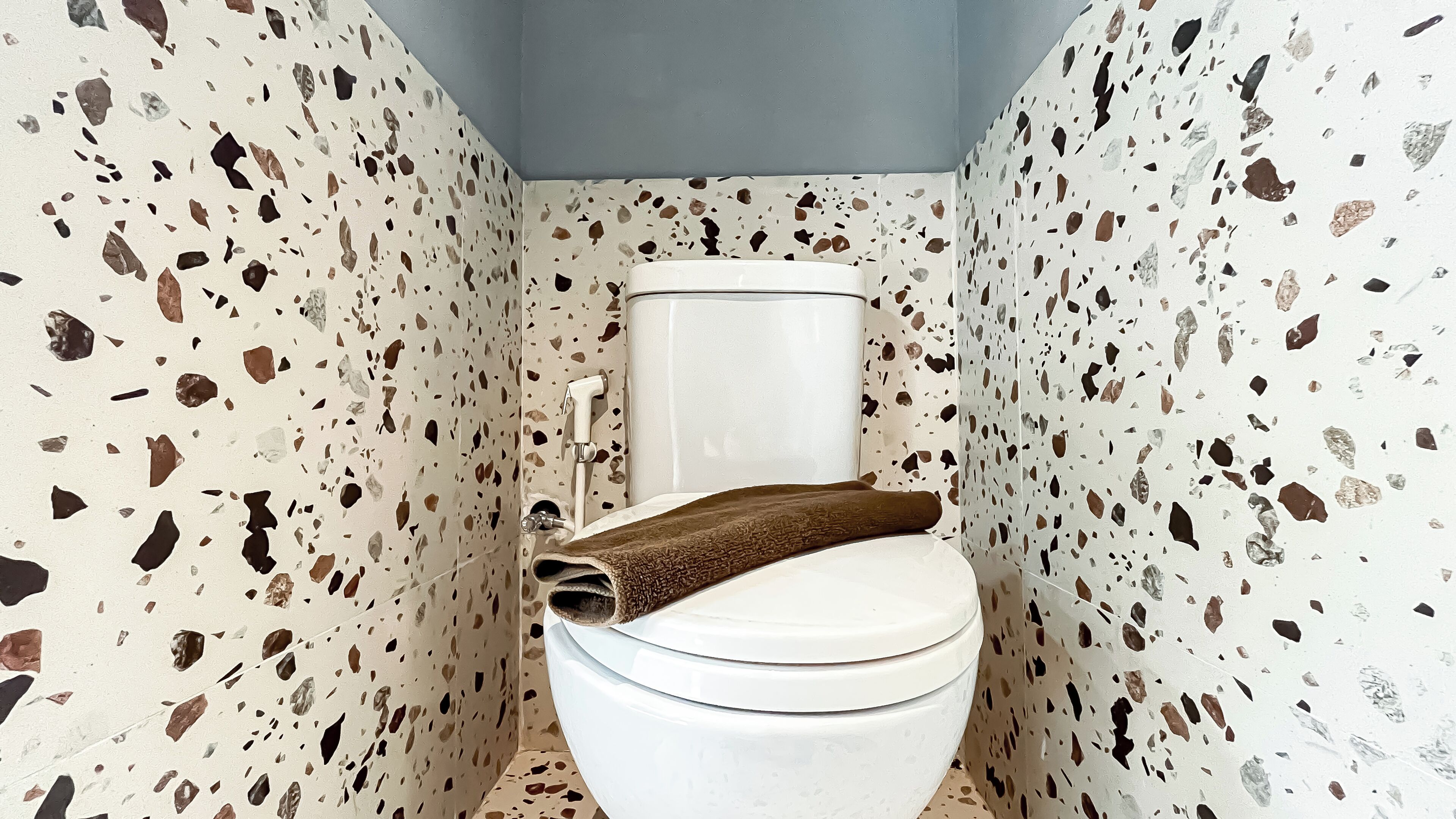 Een badkamer met een wit toilet, een bruine handdoek en terrazzovloer.