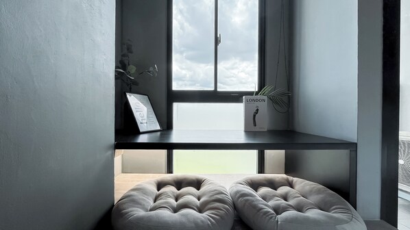 Une pièce moderne avec une fenêtre, une étagère noire, un pouf gris et une plante.