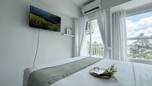 Ein Schlafzimmer mit einem Bett, einem an der Wand befestigten Fernseher, einer Klimaanlage und einem Balkon mit Vorhängen.