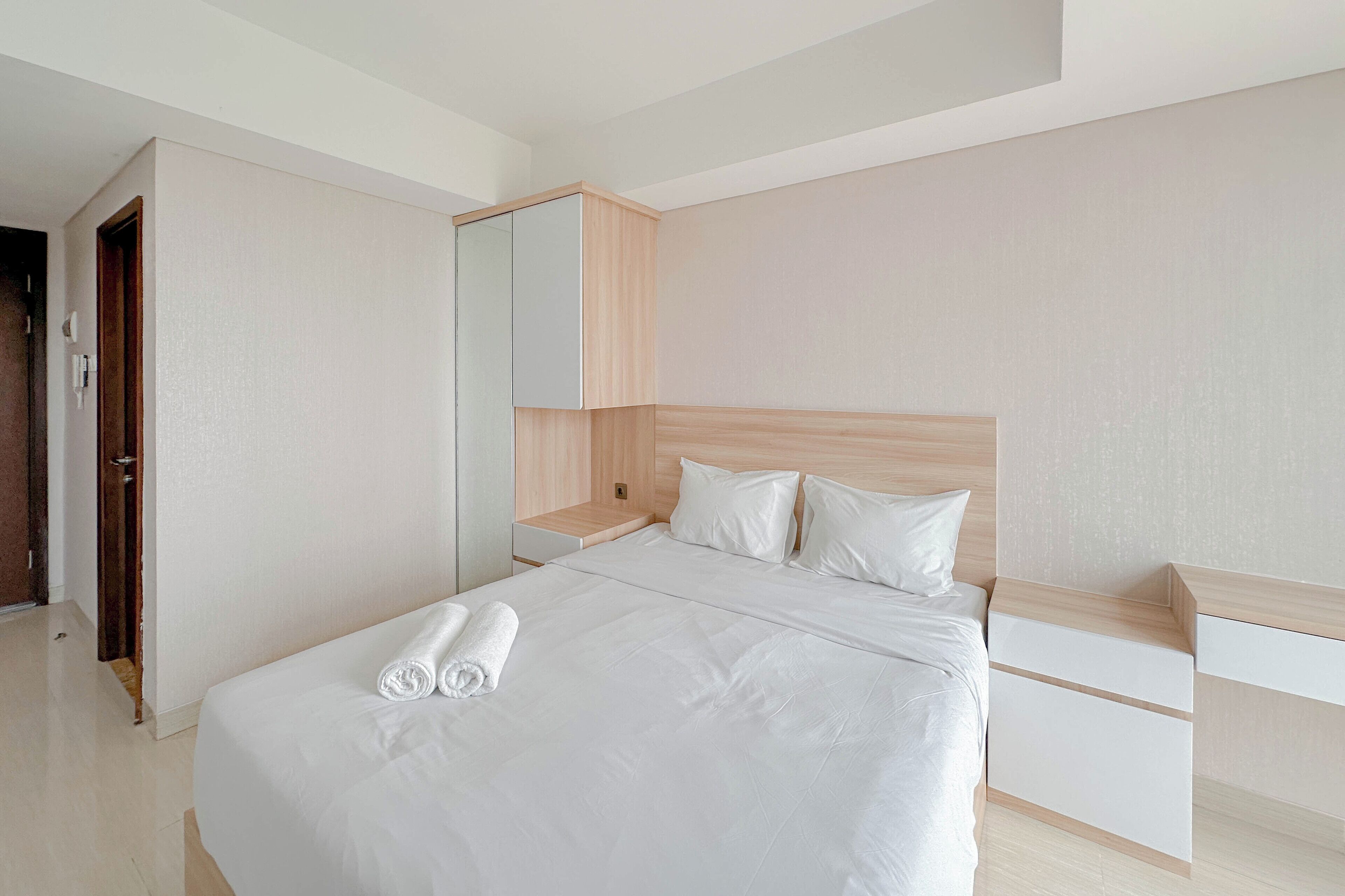 Ein modernes Hotelzimmer mit einem großen Bett, einem Holz-Kopfteil, einem Nachttisch und einem eingebauten Kleiderschrank.