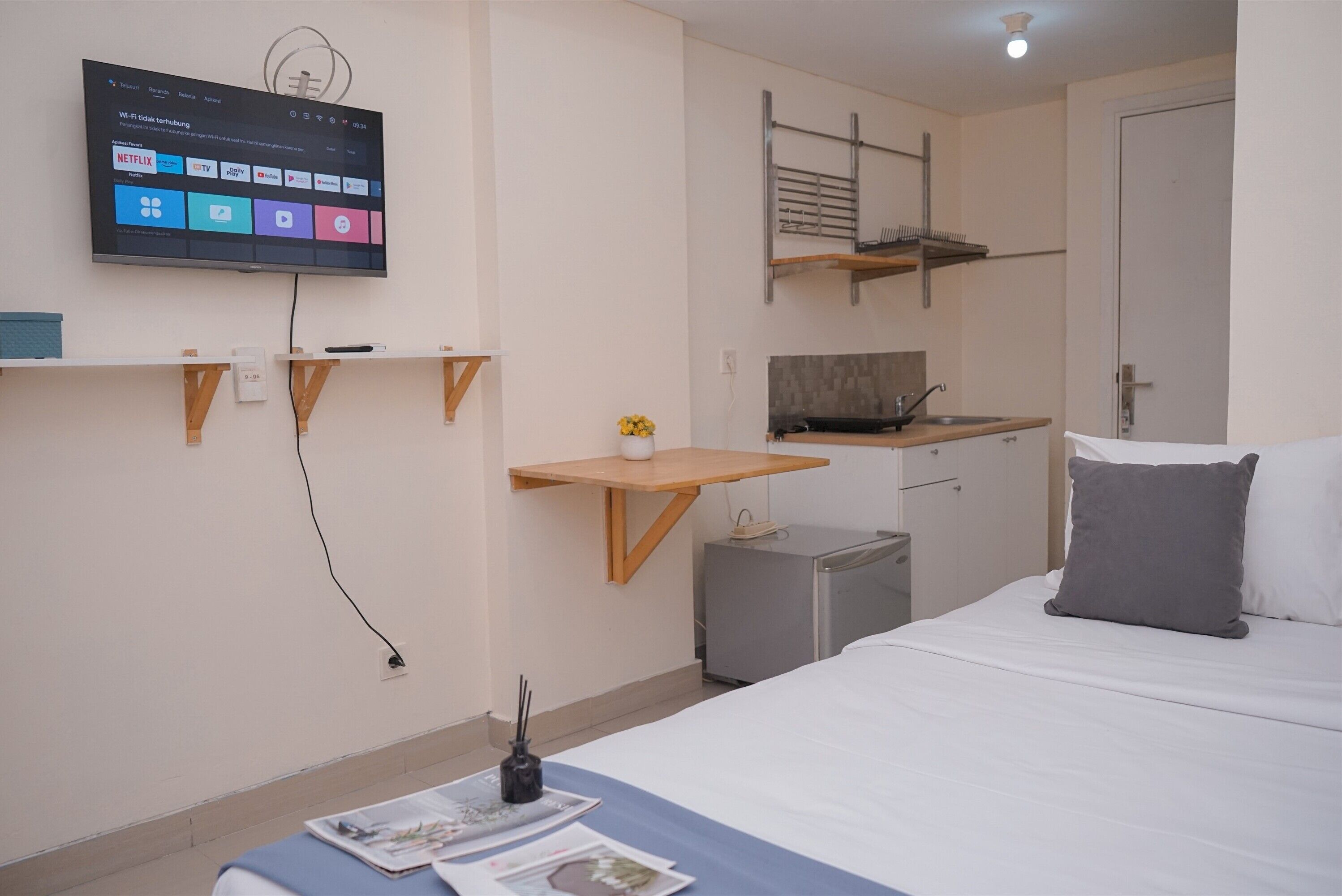 Une chambre d’hôtel moderne équipée d’un lit, d’un bureau, d’un téléviseur fixé au mur et d’une petite kitchenette.