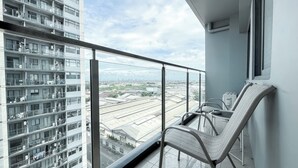 A balcony with a view of a cityscape, a chair, and a railing. - Nice and Comfortable 2BR Apartment at Daan Mogot City (Jakarta)