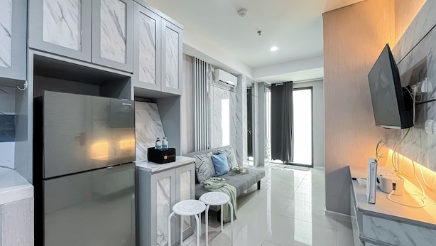 A modern kitchen with a built-in refrigerator, a flat-screen TV mounted on the wall, and a seating area with a sofa and two small tables. - Nice and Comfortable 2BR Apartment at Daan Mogot City (Jakarta)