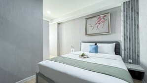 A modern bedroom with a large bed, a bedside table, a framed artwork on the wall, and a window with curtains. - Nice and Comfortable 2BR Apartment at Daan Mogot City (Jakarta)