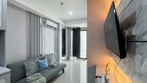 A modern living room with a grey sofa, a flat-screen TV mounted on the wall, and a large window with curtains. - Nice and Comfortable 2BR Apartment at Daan Mogot City (Jakarta)